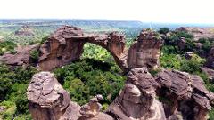 Full Day Tour To Siby And Bamako A natural rock arch frames a lush green valley dotted with trees, with rugged cliffs and distant hills under a bright sky.