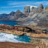Sierra Nevada del Cocuy - 7 Day Trek Here's a description of the image:A scenic view of a rocky, mountainous landscape with a blue lake partially covered in ice, under a clear blue sky.