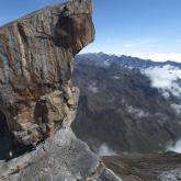 Sierra Nevada del Cocuy - 7 Day Trek Here's a description of the image:A dramatic mountain scene with a massive, jagged rock formation dominating the foreground, overlooking a vast valley and distant mountains partly obscured by clouds.
