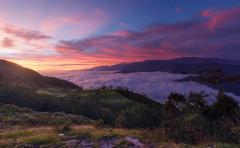 Sierra Nevada Cultural Immersion Experience (4 Days / 3 Nights) A dramatic sunrise paints the sky with vibrant pink and orange hues over a sea of clouds blanketing a mountain valley.