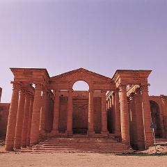 An ancient Roman temple with columns and a unique arched pediment stands tall under a clear, pale sky.