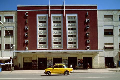 The Cinema Impero building stands with its striking facade and a yellow car parked nearby.