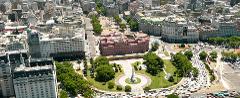 An aerial view captures the heart of Buenos Aires, showcasing the iconic Casa Rosada, lush green spaces of Plaza de Mayo, and bustling city streets packed with traffic.