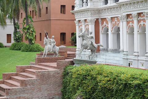 3-Day Dhaka Heritage & Culture Tour — Old Palaces, Lost Cities & Zamindari Mansions Two equestrian statues stand on stepped brick platforms in front of a building with white columns and a reddish-orange facade.
