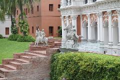 3-Day Dhaka Heritage & Culture Tour — Old Palaces, Lost Cities & Zamindari Mansions Two equestrian statues stand on stepped brick platforms in front of a building with white columns and a reddish-orange facade.