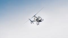 A white and black helicopter is captured in mid-flight against a pale blue sky.