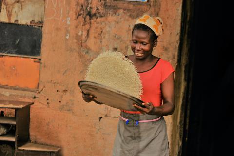 A smiling African woman is shown holding a tray overflowing with rice.
