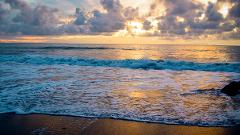 A mesmerizing sunset over the ocean, casting a golden glow on the waves and sandy beach under a sky filled with dramatic clouds.