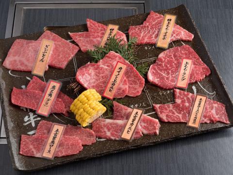 A platter of Japanese barbecue (Yakiniku) featuring various cuts of beef like loin, short rib, and rump, with some corn on the cob for garnish.