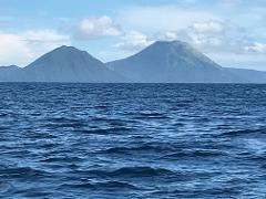 The image captures a view of the ocean with two mountain peaks in the background under a cloudy sky.