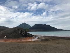 The image depicts a volcanic landscape with steam rising from the ground, a body of water in the middle, and two mountains in the background under a cloudy sky.