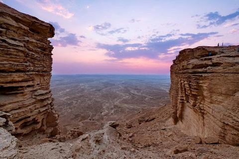 A breathtaking view of a vast desert landscape framed by towering cliffs under a colorful sunset sky.