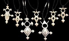 The image shows a collection of seven silver Tuareg Cross necklaces displayed against a black background, each with unique geometric designs.