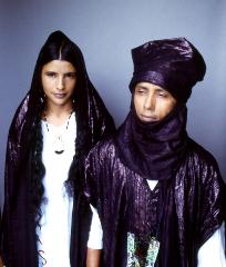 This is a portrait of a man and a woman wearing traditional clothing, including head coverings, with a plain background.