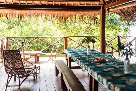 An outdoor dining area with a table set for a meal overlooks lush greenery.