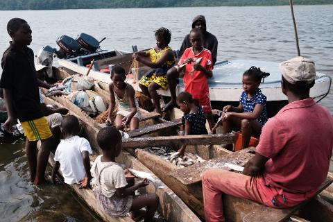 A group of people, mostly children, are in a wooden boat on the water, with some children holding fish.