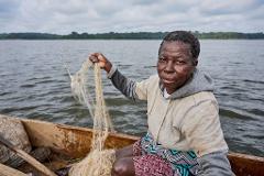 A person in a boat holds a fishing net against a cloudy sky and a distant shore.
