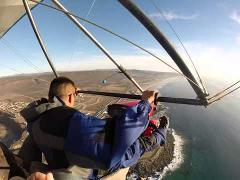 A man is hang gliding over a coastal area, offering a scenic view of the ocean and landscape below.