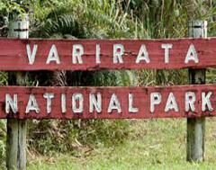 Here's a description of the image:A close-up shot of a wooden sign reading "Varirata National Park" in white letters against a red background, indicating the entrance to the park.