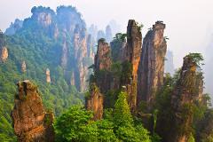 This image features towering sandstone pillars covered in lush vegetation, rising majestically from a misty, mountainous landscape.
