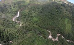 A high-angle shot shows a lush, green mountainous landscape with a waterfall cascading down the slope and a river winding through the trees.