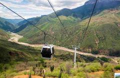 PANACHI – Chicamocha National Park A cable car travels over a river valley, with lush green mountains in the background, on a partially cloudy day.