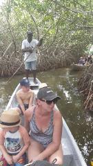 A group of people are riding in a small boat through a mangrove forest, with a man standing at the back using a pole to steer the boat.