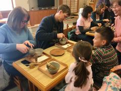 A group of people are gathered around a table, participating in a matcha making experience, with some preparing the tea while others watch.
