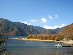 A picturesque lake with a boat docked and mountains in the background showcases autumn foliage.
