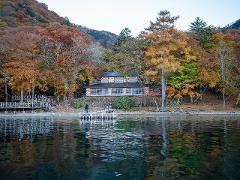 A tranquil autumn scene shows a lodge reflected in a calm lake, surrounded by vibrant fall foliage.