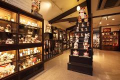A well-lit interior view of a store filled with numerous ceramic lucky cats displayed in glass cabinets and on tiered shelves.