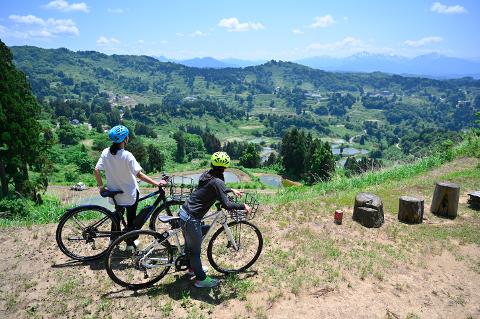 Niigata Day Trip: Explore Koi Villages & Scenic Rice Fields Two women with bicycles admire the terraced rice paddies and lush green hills of Yamakoshi, Japan.