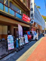 A row of colorful electric scooters and two enclosed electric vehicles are parked outside a shop in Japan.