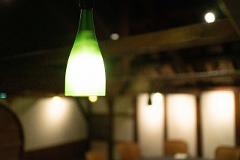 A green bottle lamp glows brightly in a dimly lit room, casting a soft light on the rustic interior.