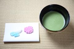 A bowl of matcha tea and two wagashi sweets sit on a tatami mat.