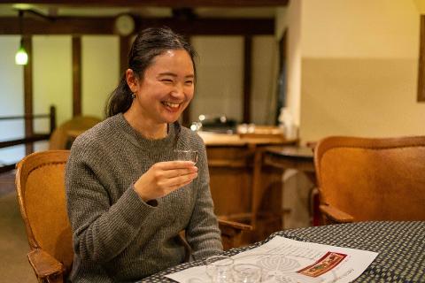 Kitakata Sake Tour: Taste & Explore Historic Brewery in a Day A woman smiles broadly while holding a small sake cup in a cozy room with traditional Japanese decor.
