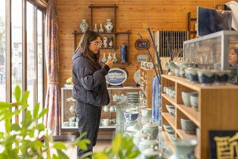 Ceramică și porțelan: Povești ale artizanilor din spatele meșteșugului A potter works at a wheel in a rustic studio, his hands shaping clay as he is illuminated by a modern desk lamp.