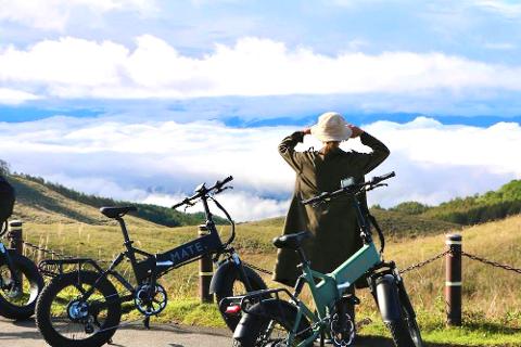 A person wearing a hat looks out at a misty mountain landscape with electric bikes in the foreground.