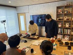 A group of people attend a Wajima lacquerware demonstration in a studio with display shelves in the background.