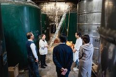 A group of people are gathered in a room with large, cylindrical containers, possibly touring a distillery or brewery.