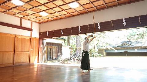 Kanazawa Castle & Kyudo Day Tour with Kaga-Style Breakfast A man in traditional Japanese attire practices kyudo in an indoor dojo with a wooden floor and ceiling.