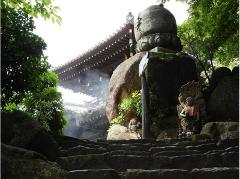 Stone steps lead up to a temple with two stone statues and a tall stone monument, enveloped in smoke and surrounded by lush greenery.