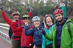 Embrace Beautiful Mother Nature on an E-Bike Tour of Yatsugatake A group of five cyclists in colorful jackets and helmets pose with raised fists, smiling at the camera.
