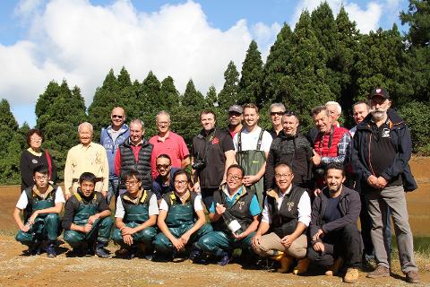 Niigata Koi Experience: Guided Nishikigoi Tour in Japan A group of people pose for a photo in front of a lush green forest, some wearing fishing waders.