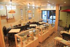 Geisha and Tea Ceremony! Experience traditional Japanese culture in Asakusa.(English Support Available) A well-lit Japanese tea shop displays pottery and tea sets in glass cases and on shelves, with seating areas arranged around tables.