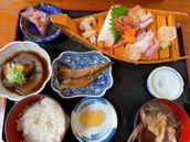 A Japanese meal featuring sashimi, stewed fish, rice, and soup is laid out on a tray.