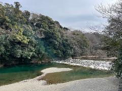 A scenic river with lush green trees on one bank and a path of stepping stones across the water under a cloudy sky.