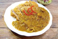 A plate of katsu curry is served on a white plate, garnished with red pepper strands, and a side of salad on a wooden table.