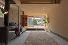 A cozy and bright living room features a wood-burning stove, a built-in bookshelf, and a large sliding glass door leading to a deck with a view of lush greenery.