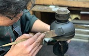 Experience 200 Years of Craftsmanship: Wajima Lacquerware Studio Tour (Visit a craftsman's home) A craftsman in Japan is applying lacquer to a black vase-like object with a wooden tool.